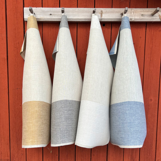 Fyra glashanddukar i linne från Växbo Lin som hänger på en trähängare som är uppsatt mot en vägg på ett rött trähus
